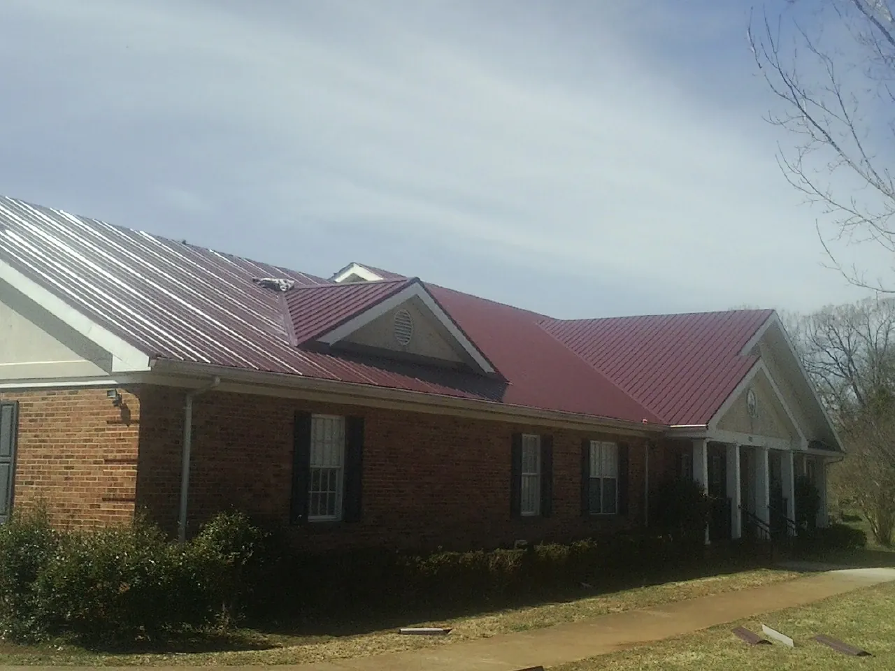 Red metal roof with gabled entries on a long brick building, from a Hail Damage Roof Repair job in Jessup