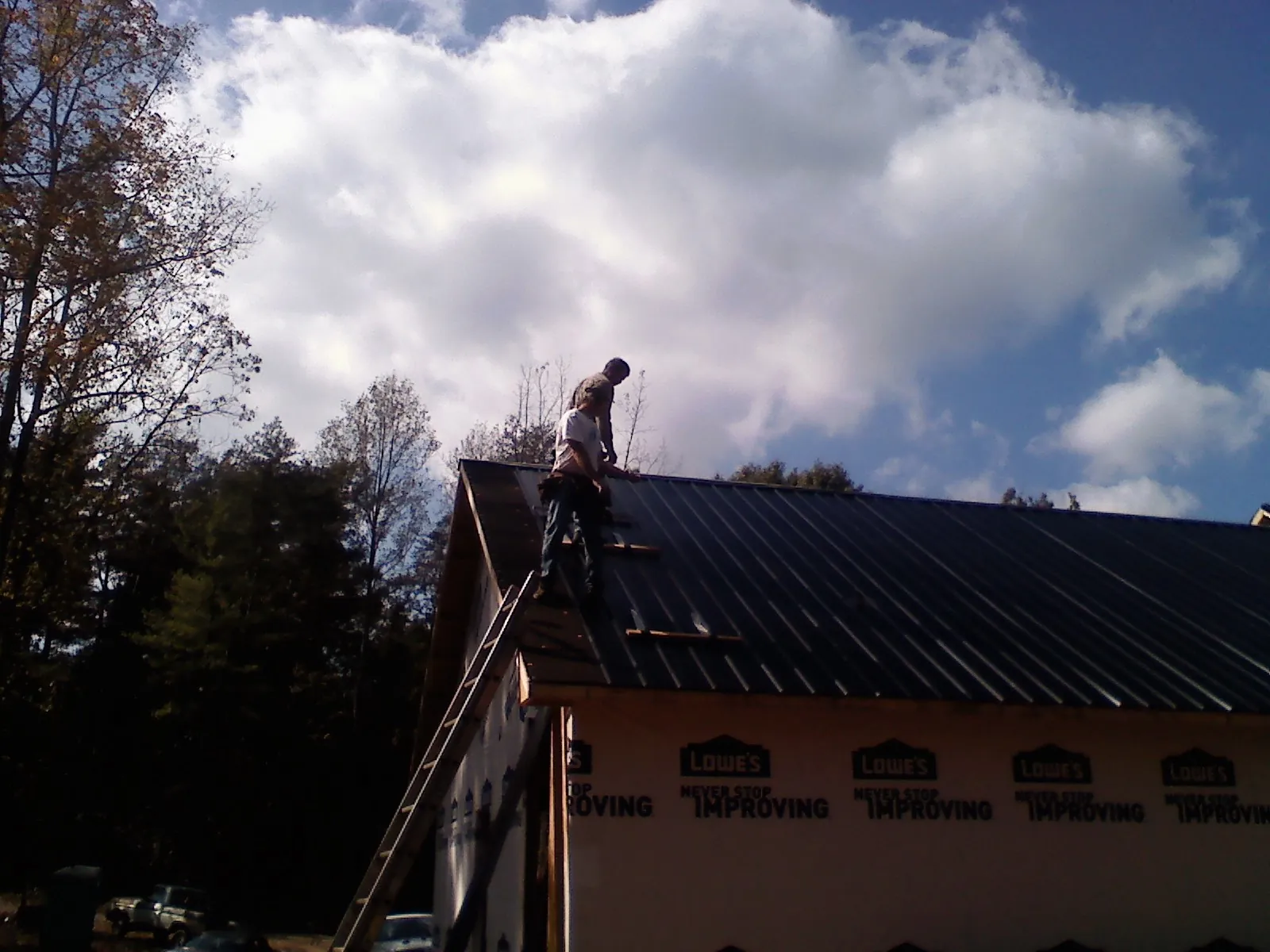 Roofer fastening dark metal panels high against a cloudy sky, from a Roof Inspection job in Jessup