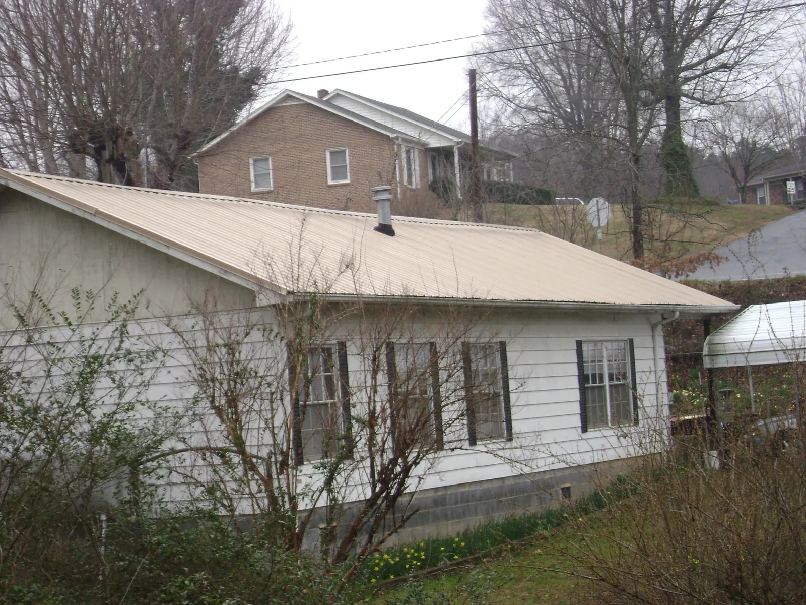 Tan metal roof on a white sided house set into a hillside — Commercial Roofing by Roofing Brothers in Jessup